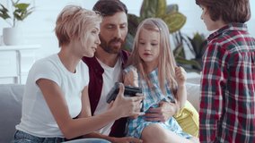 Happy caucasian parents showing photoshoot camera to their kids exploring the device together. Beautiful young family playing spending leisure at home.