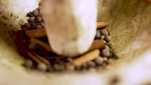 Extreme close up of a pestle crushing whole spices in a mortar in slow motion