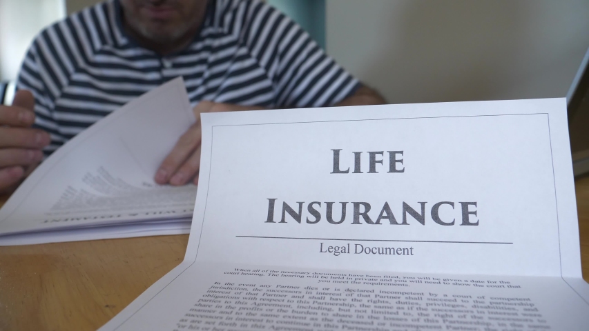 Man on the background reading and reviewing the details of a Life Insurance document. Royalty-Free Stock Footage #1057837066