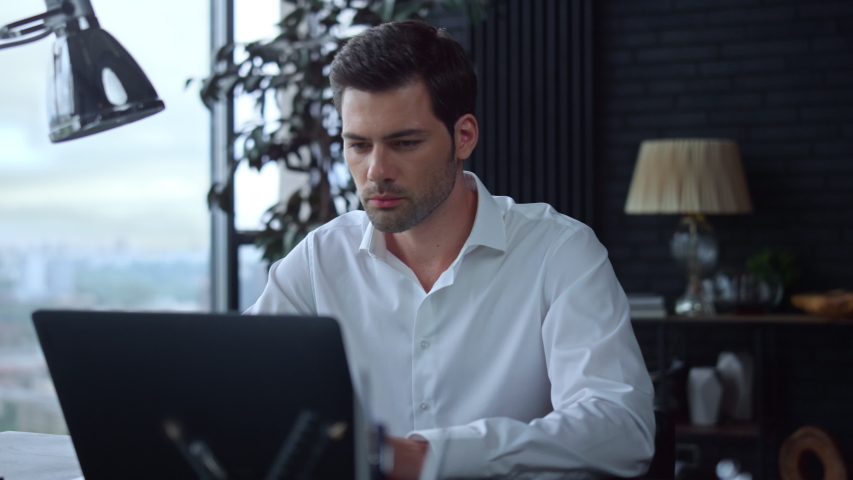 Serious businessman using laptop computer in office. Portrait of focused professional typing on laptop keyboard indoors. Young business man working on laptop at remote workplace | Shutterstock HD Video #1057837708