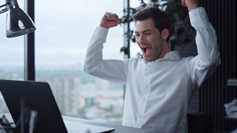 Focused businessman working on laptop computer in modern office. Surprised manager reading good news on laptop screen. Happy business man celebrating success at workplace. Man showing yes gesture
