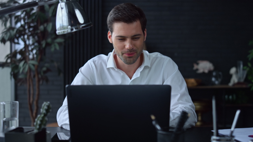 Smiling businessman working on laptop computer at home office. Male professional typing on laptop keyboard at office workplace. Portrait of positive business man looking at laptop screen indoors | Shutterstock HD Video #1057837720