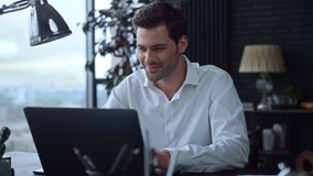 Smiling businessman working on laptop computer at home office. Male professional typing on laptop keyboard at office workplace. Portrait of positive business man looking at laptop screen indoors - Powered by Shutterstock - Get 15% off with code: PIKWIZARD15
