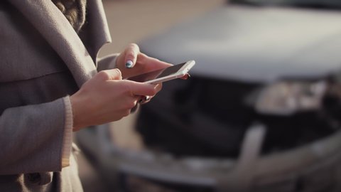woman Messaging someone in front of crashed car, close up