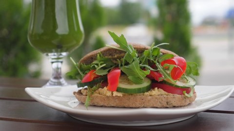 Hand serving healthy organic vegan sandwich on brown wooden table. Green smoothie with straw n long glass on the back. Healthy life style concept 