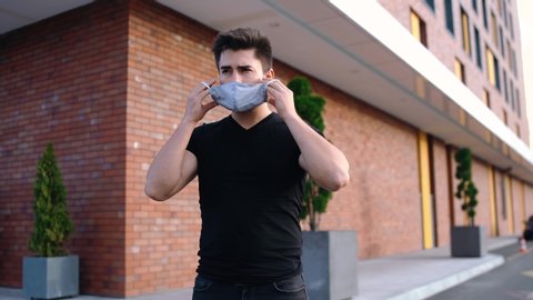 Portrait of a young man fixing his mask on his face. young man who demonstrates how to put a surgical mask on his face. Young man wearing a black T-shirt.