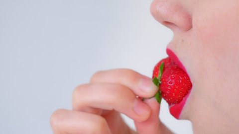 Woman with sensual red lips is eating strawberry on white background, lips closeup, side view. She has a freckles on her face. Vitamins from fresh strawberry. Unrecognizable sexy young girl.