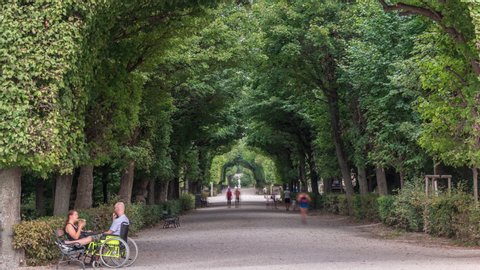 Tourists walking in park alley timelapse next to Schonbrunn Palace, imperial summer residence in Vienna, Austria. Green trees over walkway
