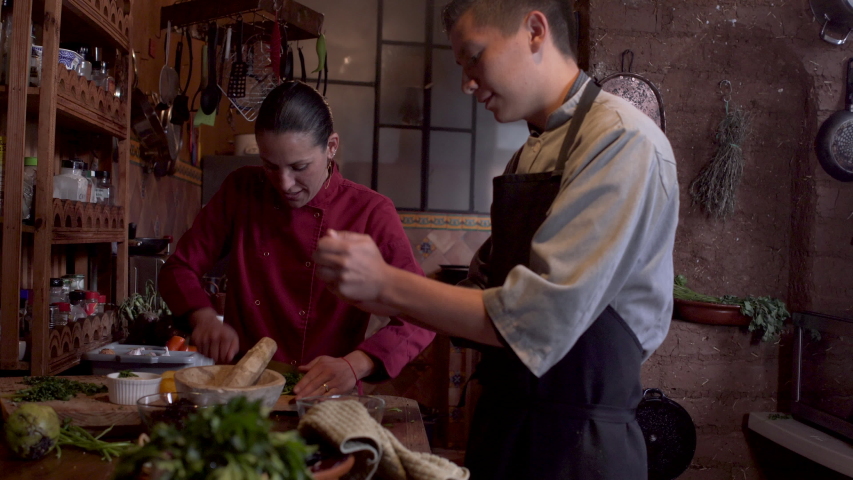 Two Latino restaurant workers including a young male assistant and female chef talking while working in a kitchen together Royalty-Free Stock Footage #1057855138