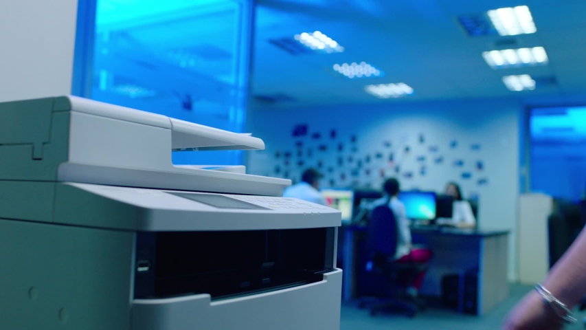 Woman using printer or scanner in office . Office worker use print machine on blurred office background with workers and computers . Hand take papers and press buttons on multifunctional copier . Royalty-Free Stock Footage #1057858507