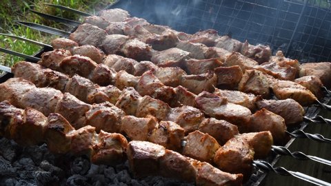 Juicy pork meat rotating on skewers over charcoal grill with smoke over. Shashlik vs Shish kebab of roasted meat traditional local food cooked on rotisserie with spits