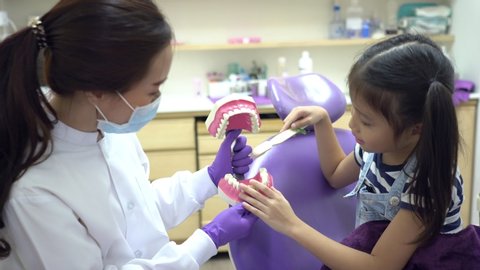 young asian dentist teach a girl to brush tooth in dental clinic