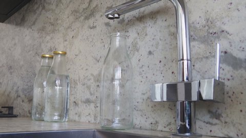 Refilling a glass bottle with filter water in a home kitchen. Reusable bottles for zero waste and sustainability. 