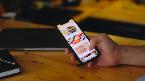 ROSTOV-ON-DON / RUSSIA - August 20 2020: Orders food using online delivery. Man orders food home in online store using a smartphone. Male ordering food from restaurant using food delivery app.