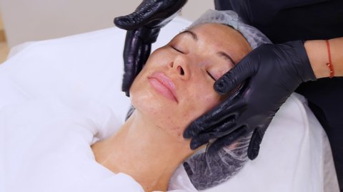 close-up, cosmetologist, in black medical gloves, performs skincare procedure, facial massage to a woman, using special cosmetic gel, in cosmetology clinic or beauty salon.