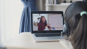 Homeschooling Asian little young girl student learning virtual internet online class from school teacher by remote meeting due to COVID pandemic. Female teaching math by using headphone and whiteboard