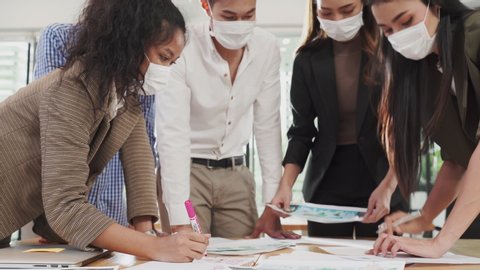 Asian teamwork business people working in office with new normal lifestyle have brainstorm meeting on table together. Group of man and woman wearing protective face mask to prevent the COVID infection