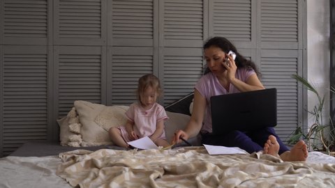 Remote Job multi-tasking mother with child. Stressed woman with laptop computer and papers working at home office
