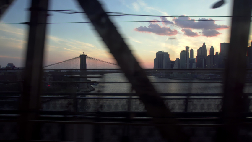 Crossing Manhattan Bridge on the Q train, sunset view over downtown New York and Brooklyn Bridge. Train Crossing. Royalty-Free Stock Footage #1057868320