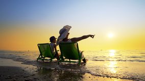 Happy family enjoy luxury sunset on the beach during summer vacations. Mother and son are sitting on a beach deck chair, against sunset, cinematic steadicam shot - Powered by Shutterstock - Get 15% off with code: PIKWIZARD15
