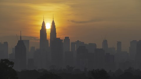 Time lapse: Silhouette of Kuala Lumpur city view during dawn overlooking the city skyline from afar with lushes green in the foreground. Federal Territory, Malaysia. Pan up motion timelapse. 