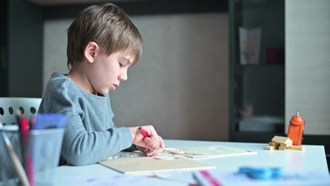 The child collects a wooden craft from parts, sitting in his room. Boy and constructor