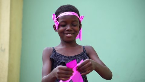beautiful African child smiling and holding pink ribbon craft in awareness of breast cancer - concept on African females and breast cancer