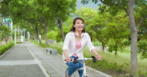 Asian female ride bicycle with headphone and smile happily in the park