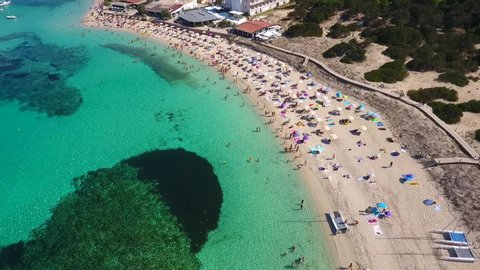 Aerial view of a private beach in Formentera island in Spain during summer season. Vacation mode fun tourism people swimming umbrella Mediterranean sea