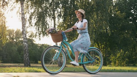 The happy cheerful woman is riding a vintage bike and enjoying outdoor leisure activity in summer. 
