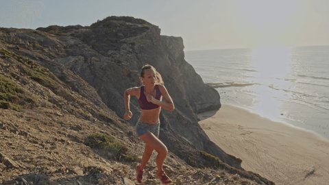 Slow motion shot of woman running on cliff above beach. Young woman jogging in nature at sunset, ocean views from above 