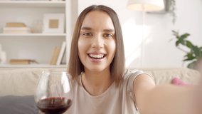 Head and shoulders portrait of attractive young woman enjoying free time at home drinking red wine and shooting selfie video on smartphone camera