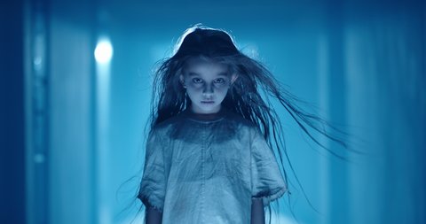Little caucasian girl in ghost white sundress costume for halloween roaring into camera, frightening someone in hallway of haunted house 4k footage