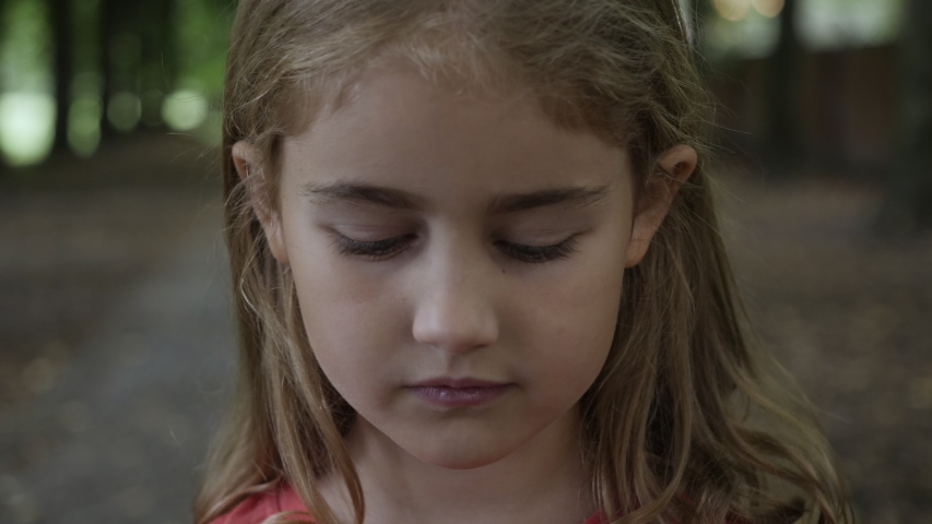 Portrait Little Child Girl Looking at Camera Standing on Street in City on Summer Day. Young Sad Thinking Curiosity Child Looking at Camera Closeup Outdoors. Face Eyes Serious Contemplative Child. Royalty-Free Stock Footage #1057890076