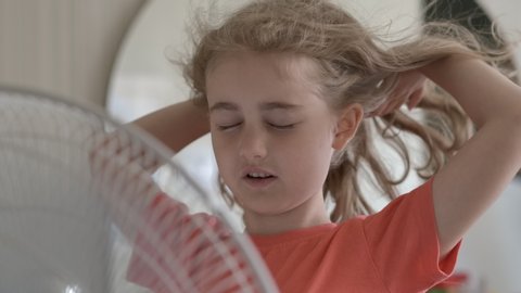 Girl Standing in Front of Fan. Child Enjoying Cool Wind From Electric Fan at Home at Summer Vacation. Suffer From Heat High Temperature in Front of Ventilator Cooling Herself With Electric Fan-Cooler.