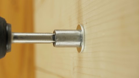 Screwdriver screw lag bolt in a wooden wall. Electric drill screws the lag bolt in a wooden surface, vertical close-up view.