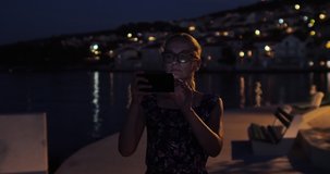 A woman with glasses takes a photo with her mobile phone. Warm summer evening by the Adriatic Sea in Postira on the island of Brac.
