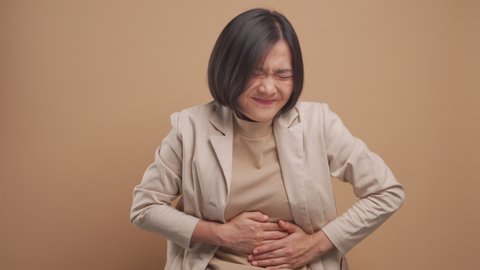 Asian business woman was sick with stomach ache and standing isolated over beige background. 4K video