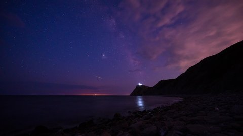 Amazing time lapse with Milky Way galaxy, moving clouds, plane trails and meteor shower, during Perseid stream over rocky Black sea coast and cape Emine with the lighthouse, Bulgaria