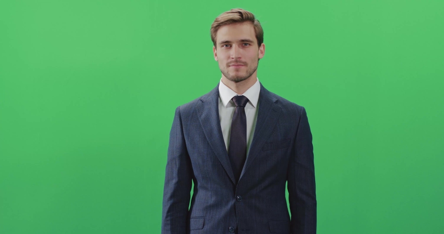 Businessman in a suit standing in green room and looks at the camera, chroma key background, a man smiles, positive emotions. Royalty-Free Stock Footage #1057895419