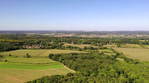 4K aerial drone footage approaching rural village amongst woodland and farm fields in countryside, West Berkshire, UK