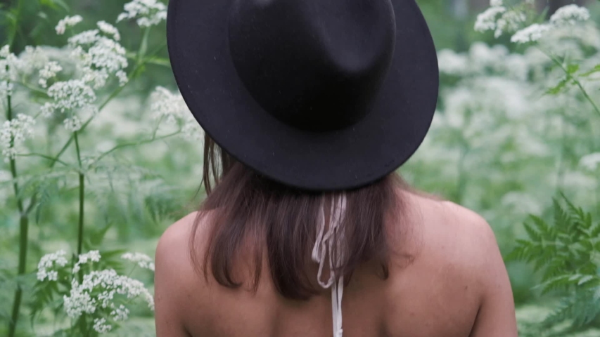 Young beautiful woman in a hat walks in the deep forest outdoors among white flowers