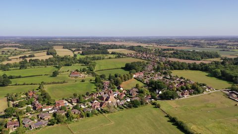 4K aerial drone footage moving backwards away from a rural village amongst farm fields and woodland in English countryside, West Berkshire, UK