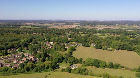 4K aerial drone footage moving backwards away from a rural village amongst woodland and farm fields in countryside, West Berkshire, UK