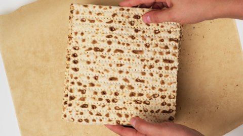 two female hands place a baked square matzah on brown parchment paper, top view. Ingredient for the festive Easter meal of the Seder