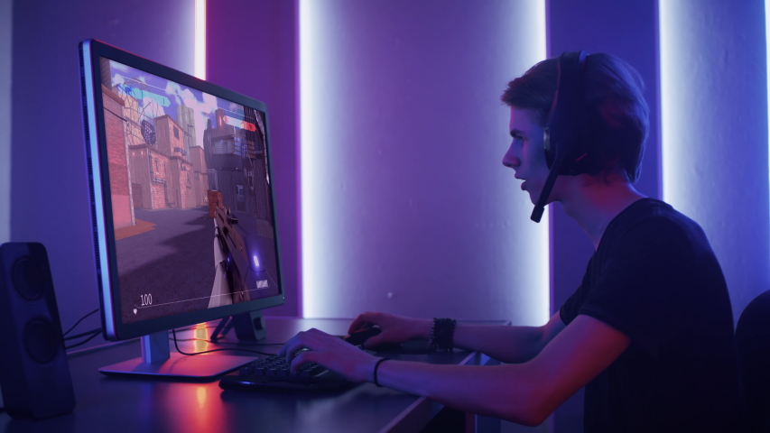 Professional eSports Gamer Skilfully Plays 3D Shooter Mock-up Video Game with Super Action and Fun Special Effects on His Computer, Talks to Teammates using Headset. Cyber Gaming Retro Neon Room