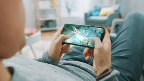 Point of View Shot Man Playing Mockup- MOBA RPG Game on his Smartphone while resting at Home on a Couch. Cool Game with Modern Graphics and Fun Gameplay. Cyber Gaming