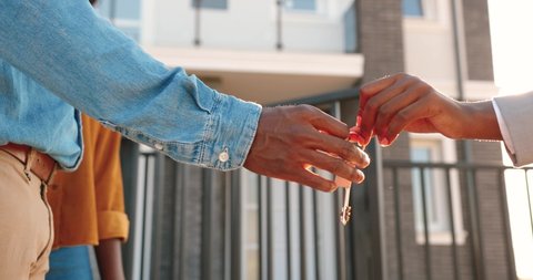 Close up of African American female hand passing key to male outdoors in sunlight. Woman handing keys of new house to man customer. Buying dwelling. Selling home. Real-estate agent job.