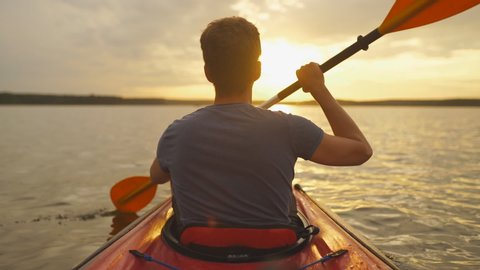 Meeting sunset on kayaks. Rear view of young man kayaking on lake with sunset in the background : vidéo de stock