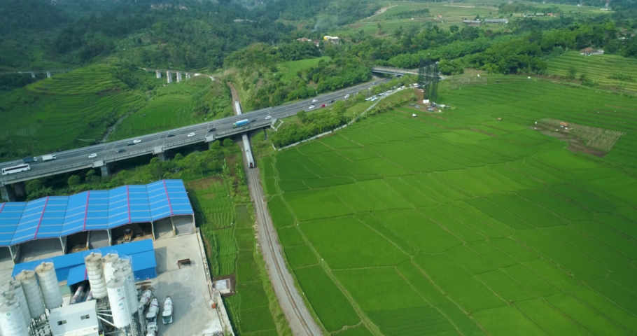 Scenic aerial view of passenger train passing by a curved rail and rice  field near cimeta bridge and cipularang toll road, bandung, west java  indonesia